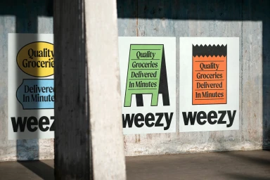 Posters featuring Weezy branding and typographic grocery designs pasted on a concrete wall in daylight