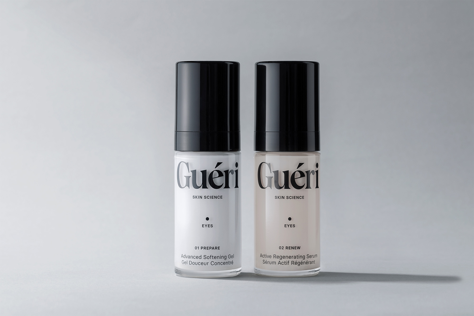 Two bottles of Guéri Skin Science eye serum, one 'Prepare' and one 'Renew,' stand against a soft gray backdrop in a beauty product shot.