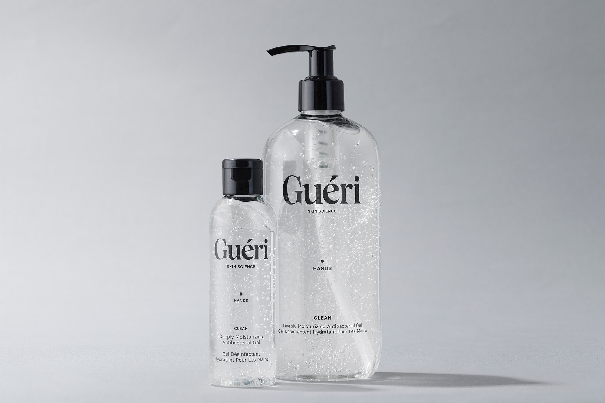 Two clear bottles of Guéri hand sanitizer in varying sizes stand on a white surface, showcasing the skincare product against a simple background.