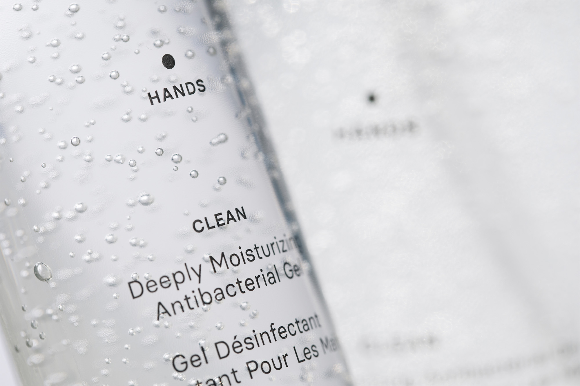 Close-up of clear hand sanitizer bottle with bubbles; label reads “HANDS CLEAN Deeply Moisturizing Antibacterial Gel”, on a white background.
