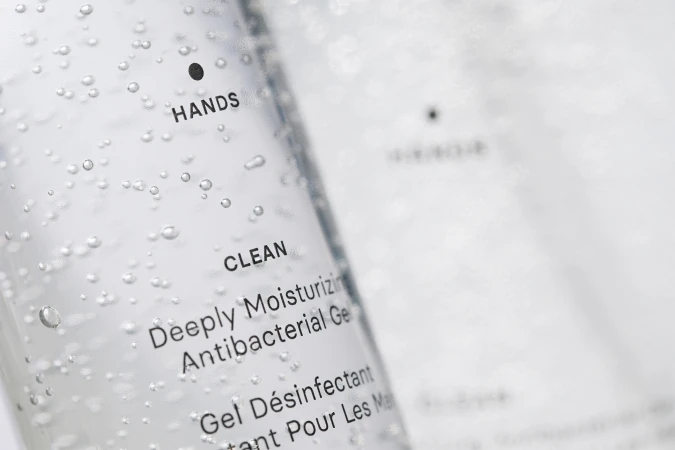 Close-up of clear hand sanitizer bottle with bubbles; label reads “HANDS CLEAN Deeply Moisturizing Antibacterial Gel”, on a white background.