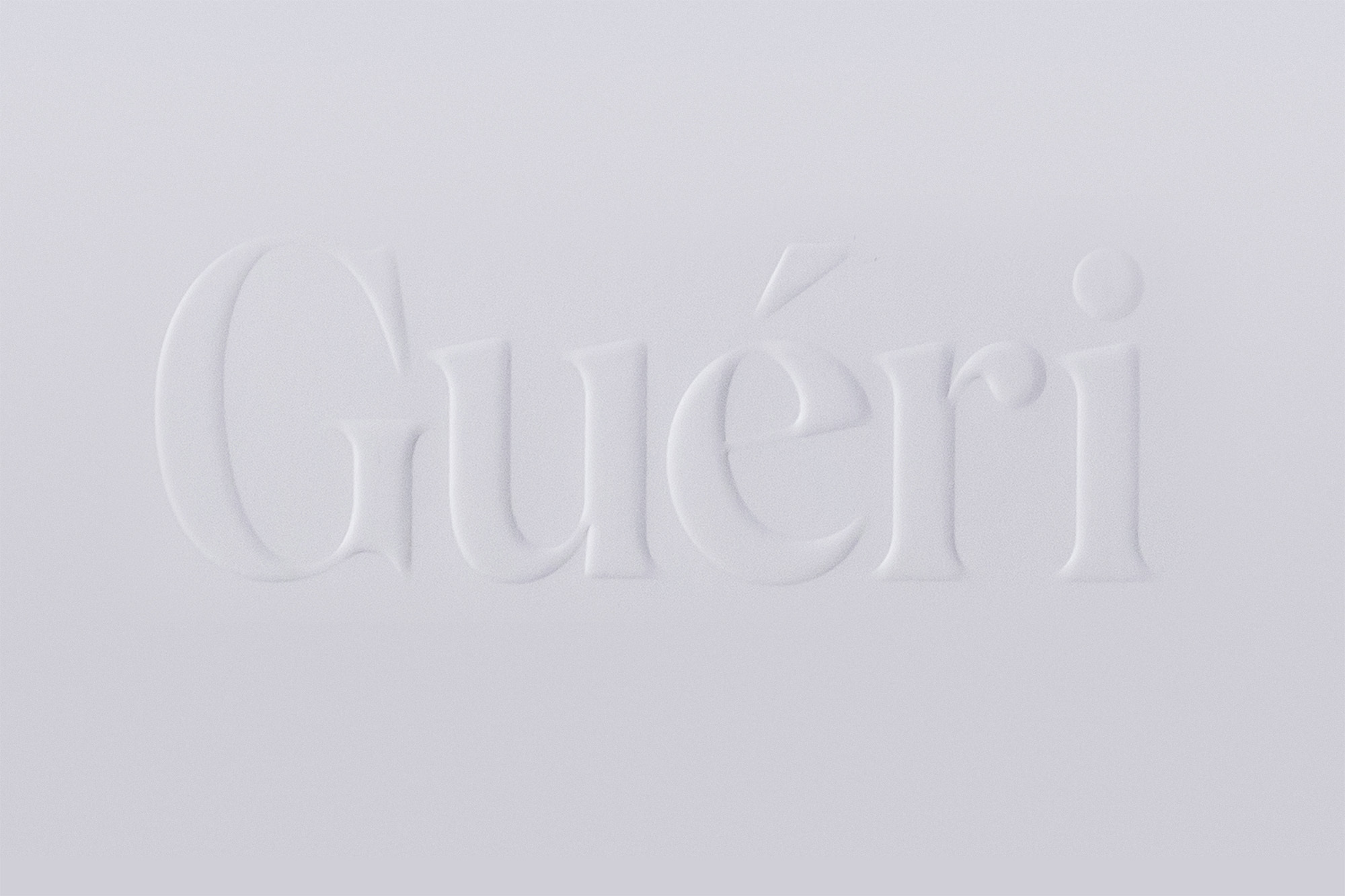 Close-up of the embossed text "Guéri" on a clean, white surface. The monochromatic design highlights subtle shadows and elegant typography.
