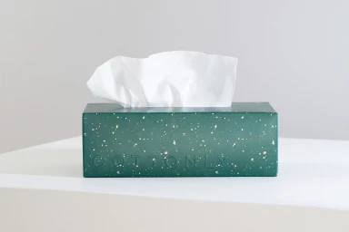 Green speckled tissue box with white tissues dispensing from top against light background