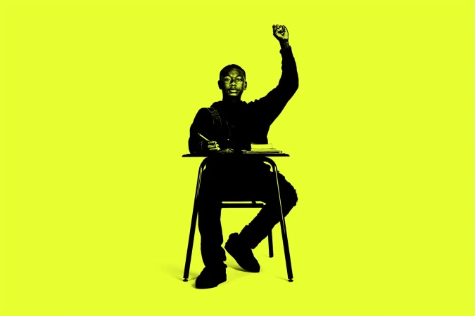 Silhouette of student sitting at desk with raised fist on yellow background. Person writing, classroom chair and desk.