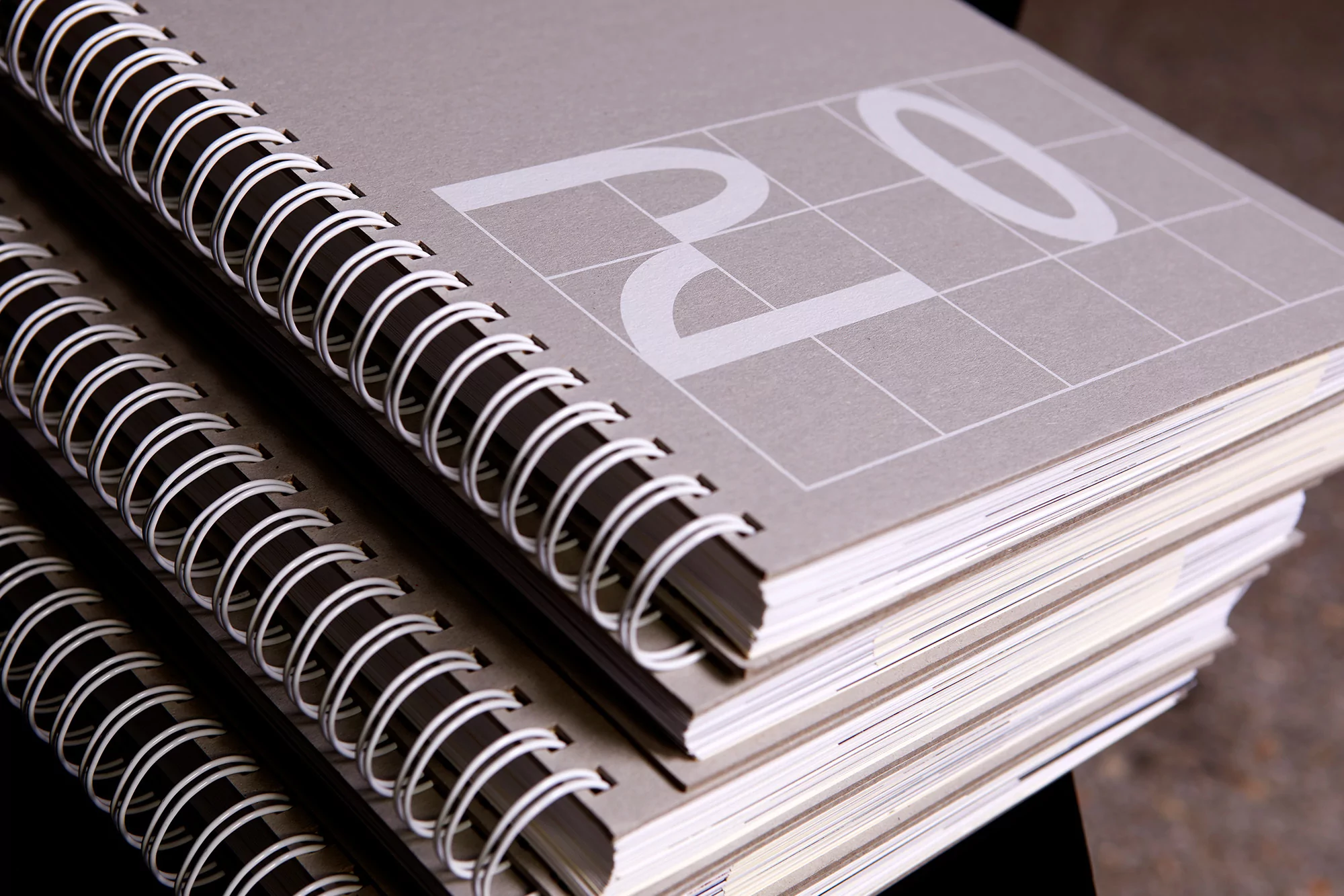Stack of wire-bound notebooks with a grid pattern and large white letters on their gray covers, presenting a minimalist, organized aesthetic.