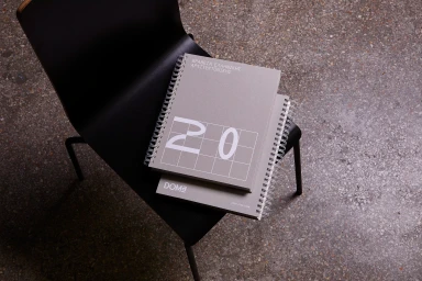 Two grey spiral-bound publications resting on a black modern chair over a speckled terrazzo floor.