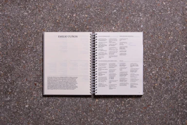 An open spiral-bound book featuring Greek typography and text layouts displayed on a speckled stone surface.