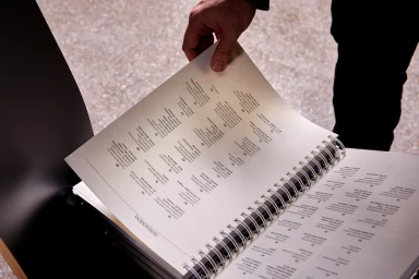 Person holding a spiral-bound book showing a table of contents page with numbered architectural entries in an outdoor setting