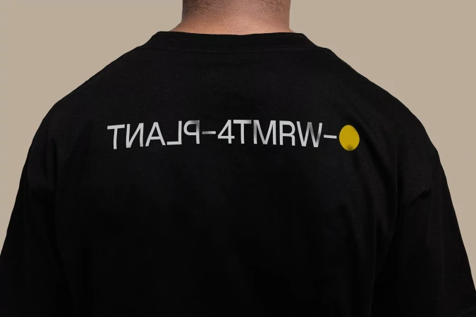 Black t-shirt featuring backwards silver lettering 'TИA⅃q-4TMRW-' and a yellow dot on the upper back, center frame.