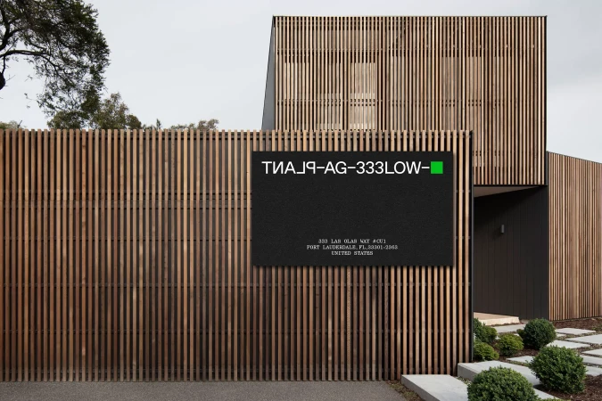 Modern wooden slat building exterior featuring a dark rectangular sign with white lettering and a green square for PLANT Agricultural Systems