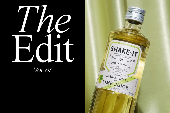Still life shot of a 'Shake-It' cordial mixer bottle with lime juice against draped green fabric, adjacent to graphic text on black.