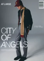 Model wearing a black jacket, grey trousers, patterned scarf, and maroon baseball cap against a grey studio background