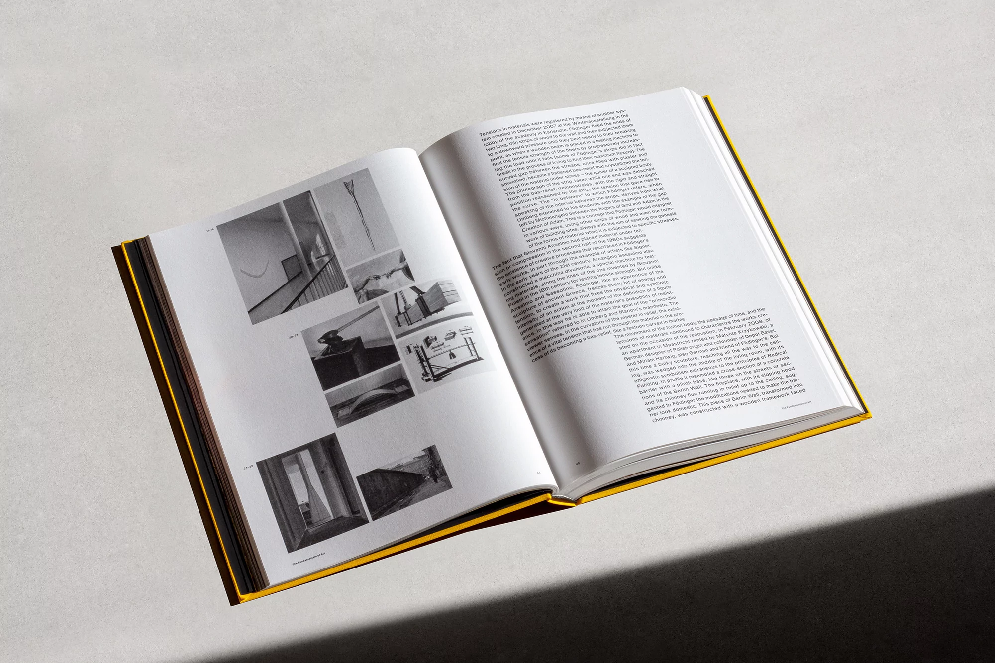 Open book with architectural photography and text pages, laying flat on a gray surface with a shadow cast across the lower right corner.