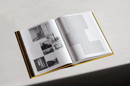 Open hardcover book with yellow spine showing printed text pages and black-and-white photographs on a light background