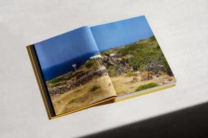 Open hardcover book resting on a neutral grey concrete surface, displaying a landscape photograph across its pages.