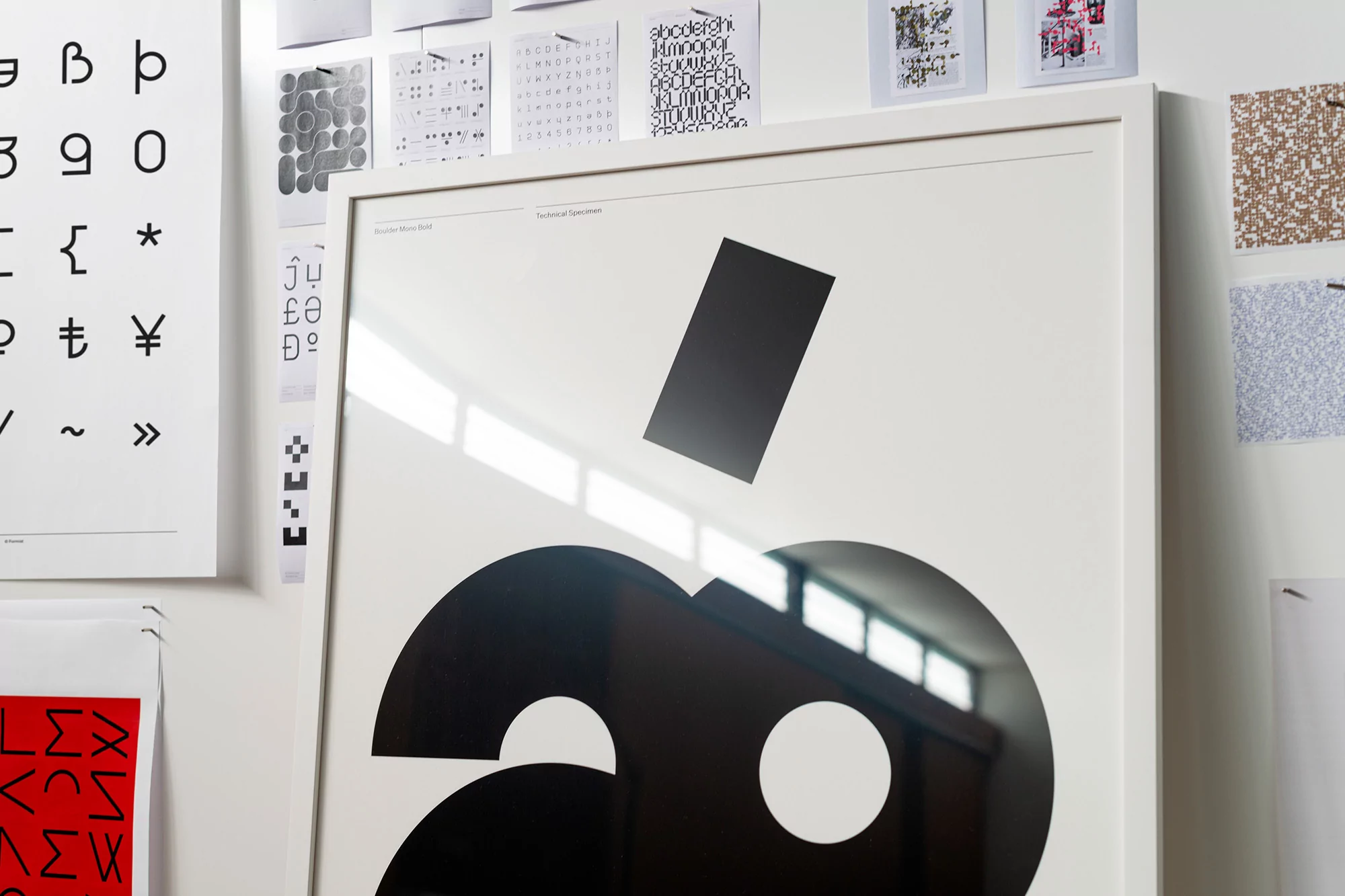 Abstract design poster featuring black geometric shapes on a white background, framed in white, displayed on a white wall with text-based prints.