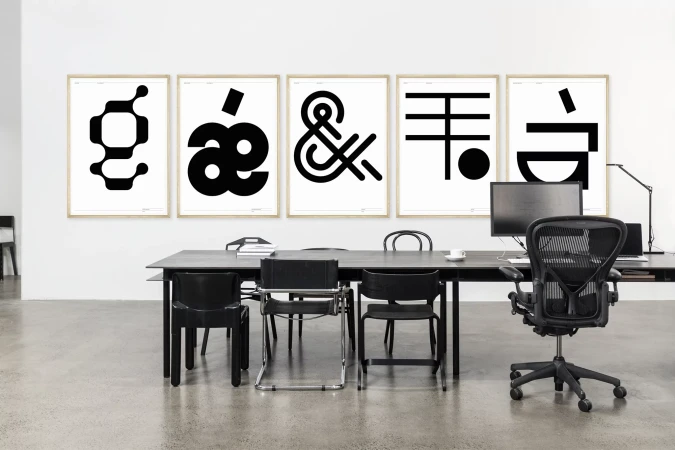 Office space featuring black desk, black chairs, a computer, and framed typographic prints in a minimalist, modern interior setting.