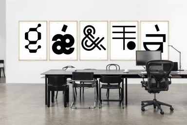 Minimalist office interior featuring a long conference table and five framed black and white abstract graphic posters on the wall.