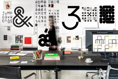 A motion-blurred person walking past a white wall covered in black graphic posters and typography prints in an office setting.