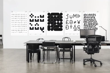 Five black and white typography posters displayed on a white wall above a long modern meeting table and chairs