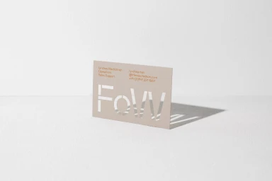 Beige business card featuring white cutout lettering casting a sharp shadow on a white seamless studio backdrop.