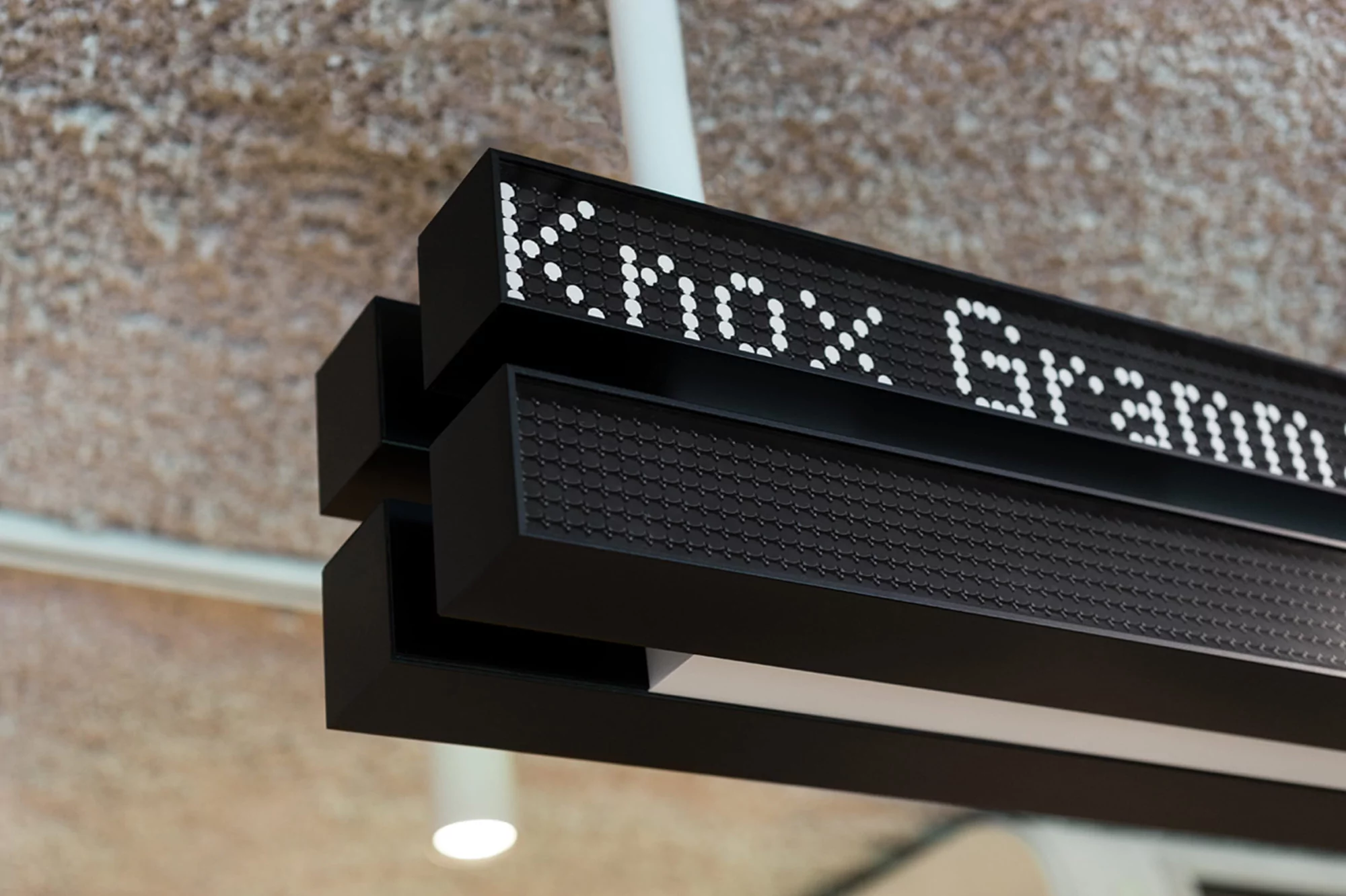 Illuminated sign displaying the text 'Knox Grammar' with white dots on a black rectangular panel, mounted on a ceiling structure.