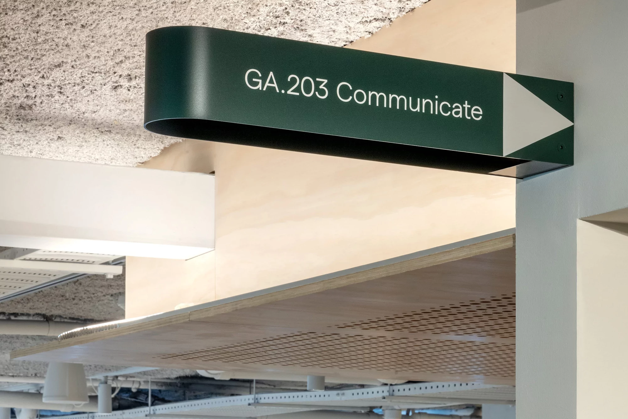 Indoor wayfinding sign with 'GA.203 Communicate' in white text on a green background with a white arrow pointing right.