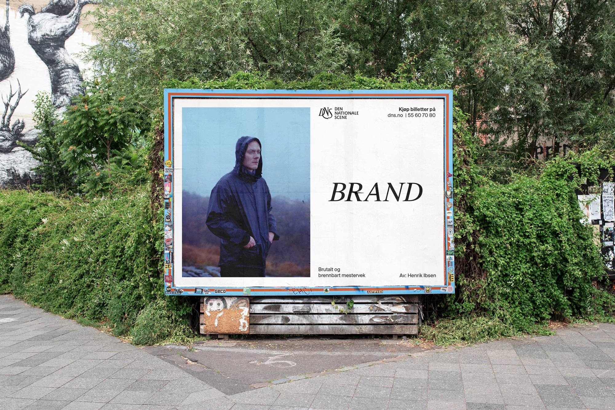 Outdoor advertising billboard featuring a hooded figure in a jacket against a foggy backdrop, surrounded by greenery in an urban setting.