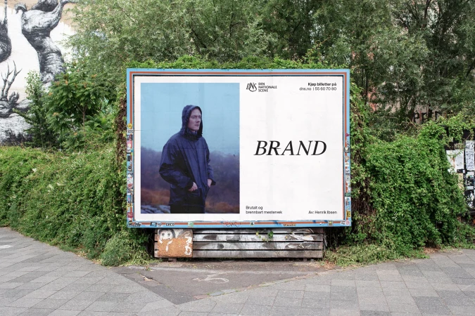 Outdoor advertising billboard featuring a hooded figure in a jacket against a foggy backdrop, surrounded by greenery in an urban setting.