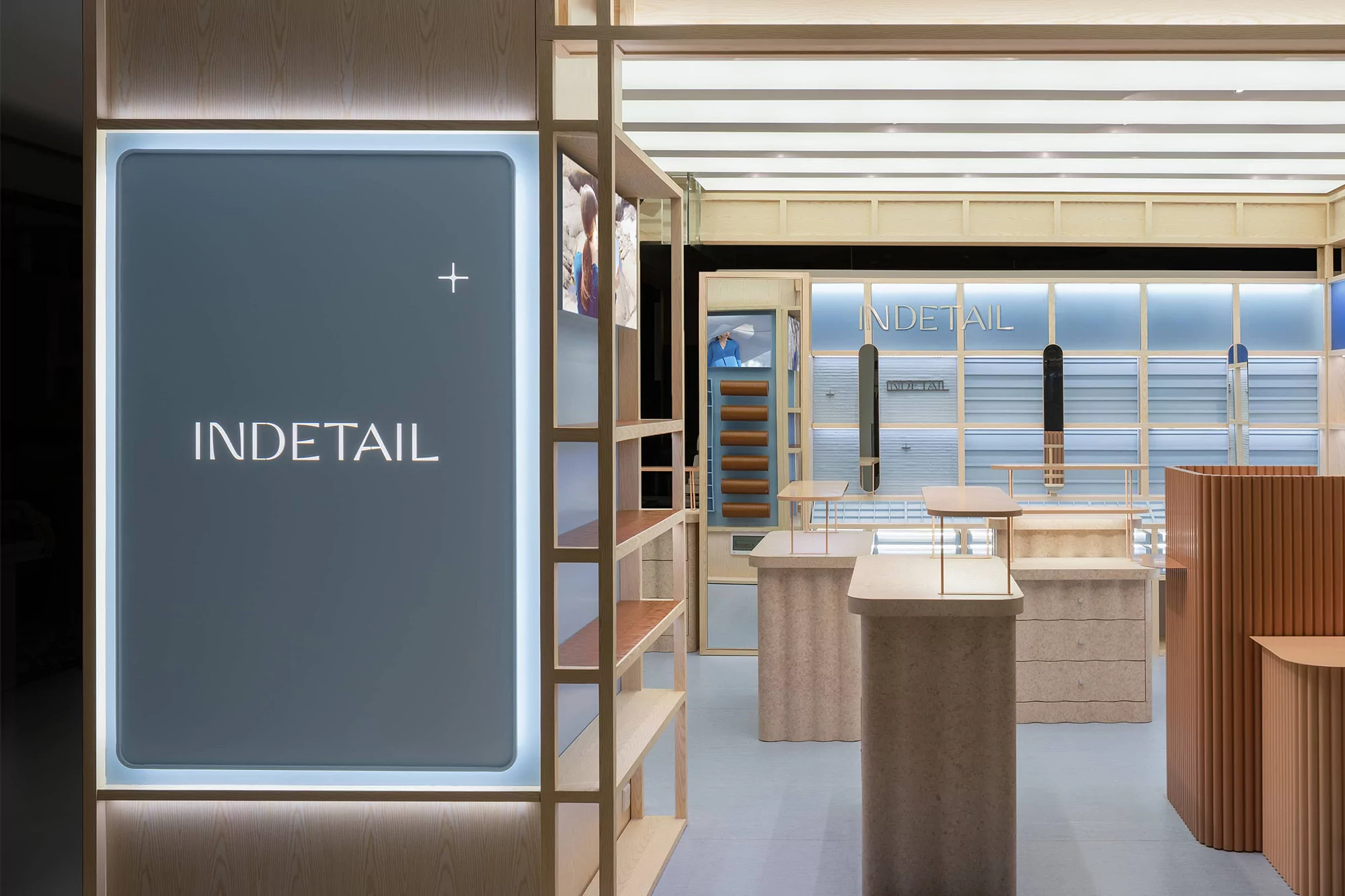 Interior design of a retail store with light wood shelves, product display cases, and an illuminated sign reading INDETAIL.