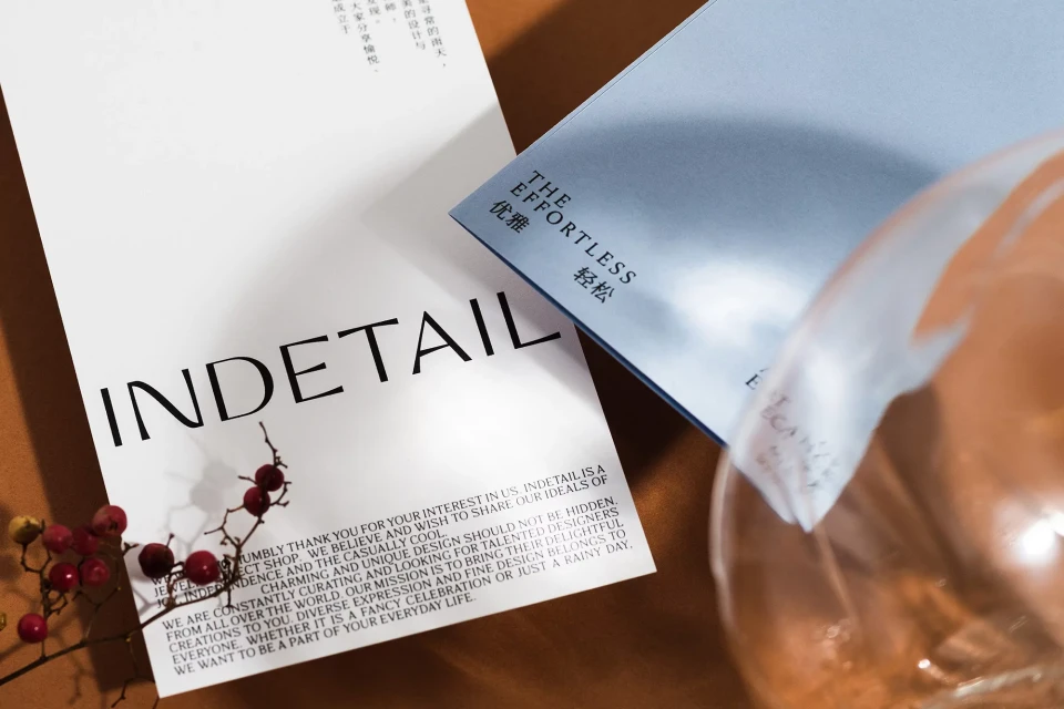 Promotional product shot featuring a product card, flowers, and a glass prop, set on a brown surface with soft, diffused lighting.