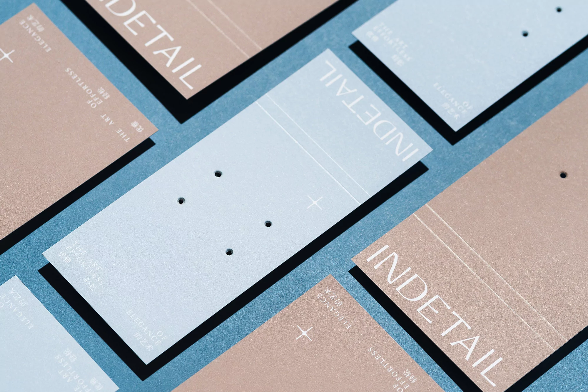 Close-up of pastel-colored earring display cards with minimalist typography and geometric accents against a soft blue background.