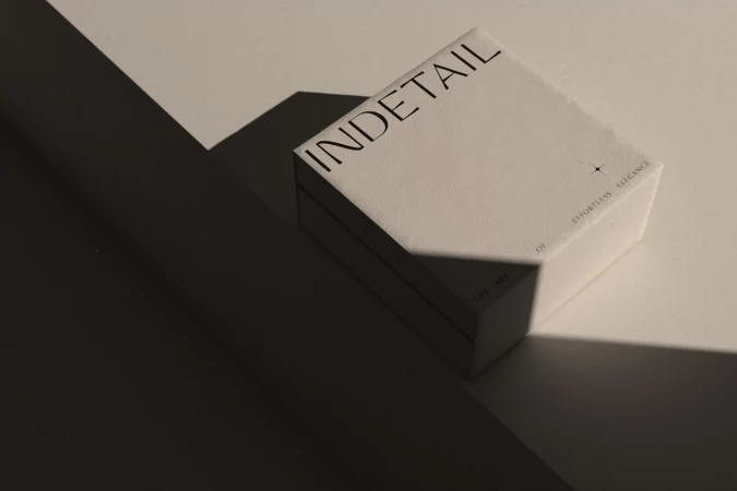 Rectangular white product box for INDETAIL brand on a white surface with stark lighting and shadows, minimalist product photography.