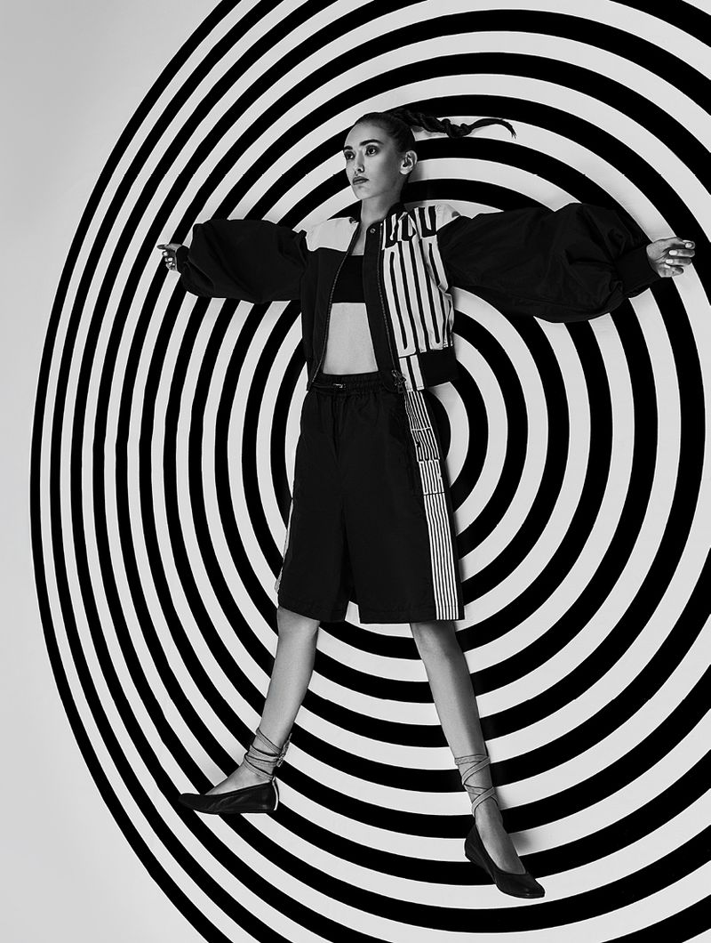 Fashion shot of a woman posing in black and white sportswear against a concentric circle backdrop in a photo studio setting.