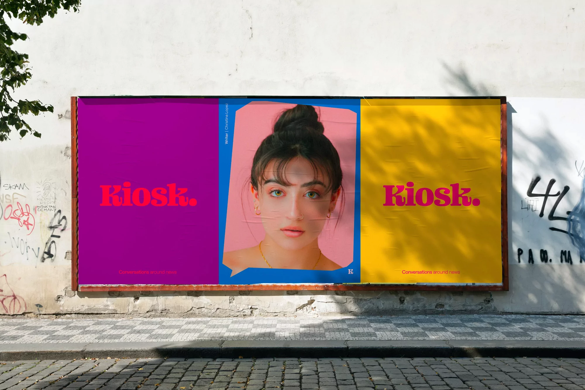 Outdoor poster on a building featuring a woman's face and 'Kiosk.' text in vibrant magenta, yellow, and purple panels on a stone wall.