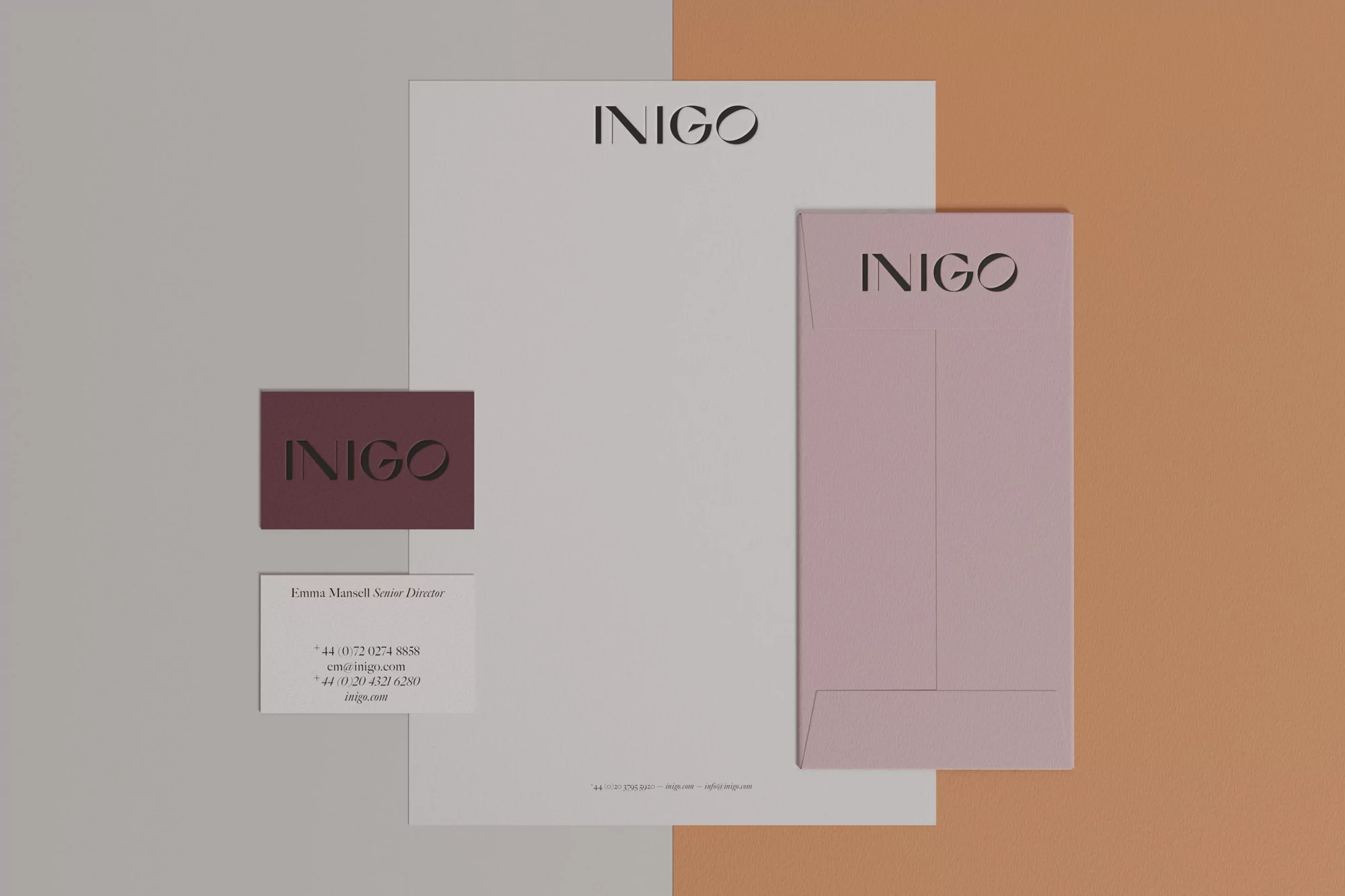 Flat lay of 'INIGO' stationery set including letterhead, business card and envelope, on a two-tone background of gray and tan.