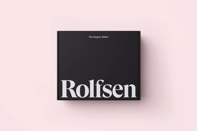 Top-down view of a black square packaging box with white typography branding set against a pale pink background