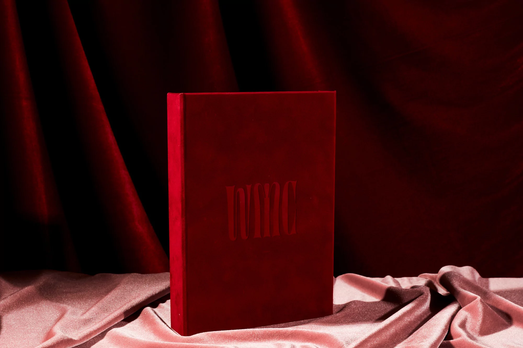 Still life of a red box, possibly a book or photo album, resting on a peach satin fabric against a red and black draped background.