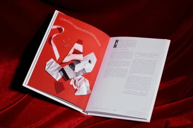 An open book with red and white pages featuring collage artwork and typography, resting on a deep red velvet fabric surface.