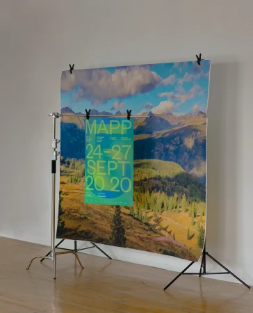 A photo studio setup featuring a backdrop with a landscape image and a poster hanging in front, supported by metal stands against a white wall.