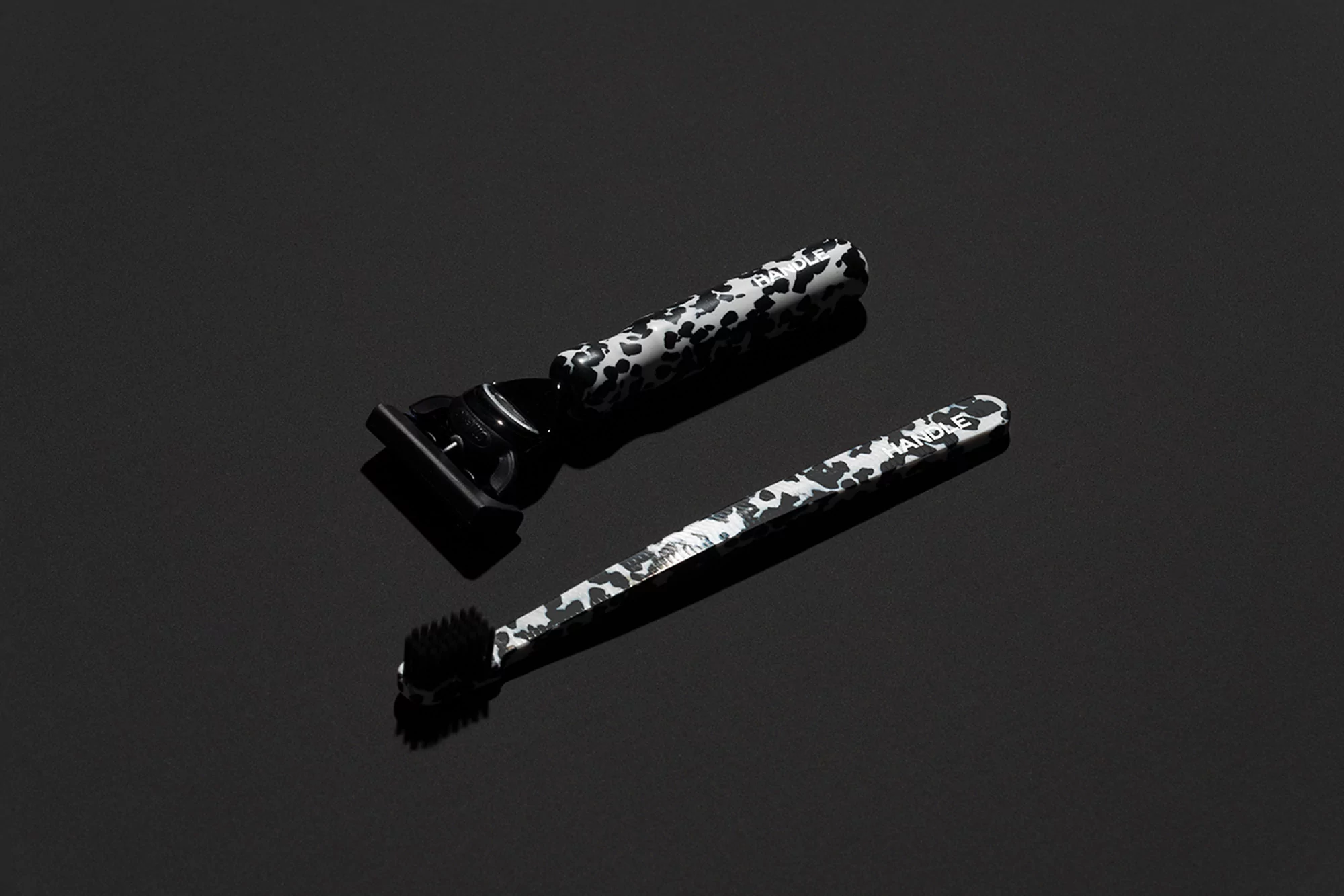 Close-up of a safety razor and brush with speckled handles on a glossy black surface, studio lighting, dark background, beauty concept.