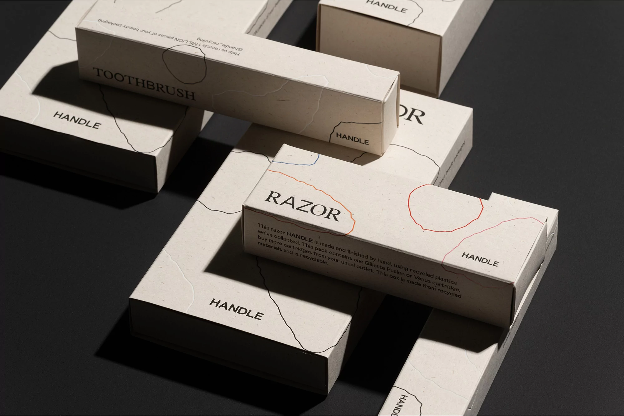 Multiple rectangular boxes, labeled 'Razor' and 'Toothbrush,' are arranged on a dark surface, displaying sustainable packaging for personal care.