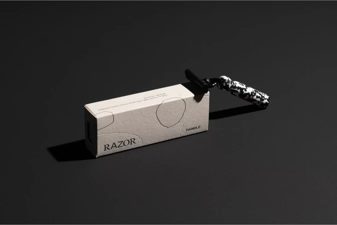 Product packaging for Handle razor with a black and white patterned handle resting on a grey surface