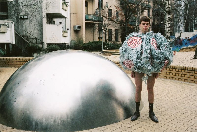 Person in a unique costume with a large silver dome structure in an urban setting. Building and play area visible in background.