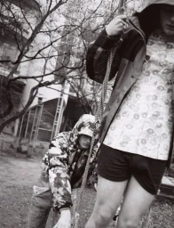 Black and white editorial image of two models outdoors with trees and a rope swing, featuring floral patterned clothing.