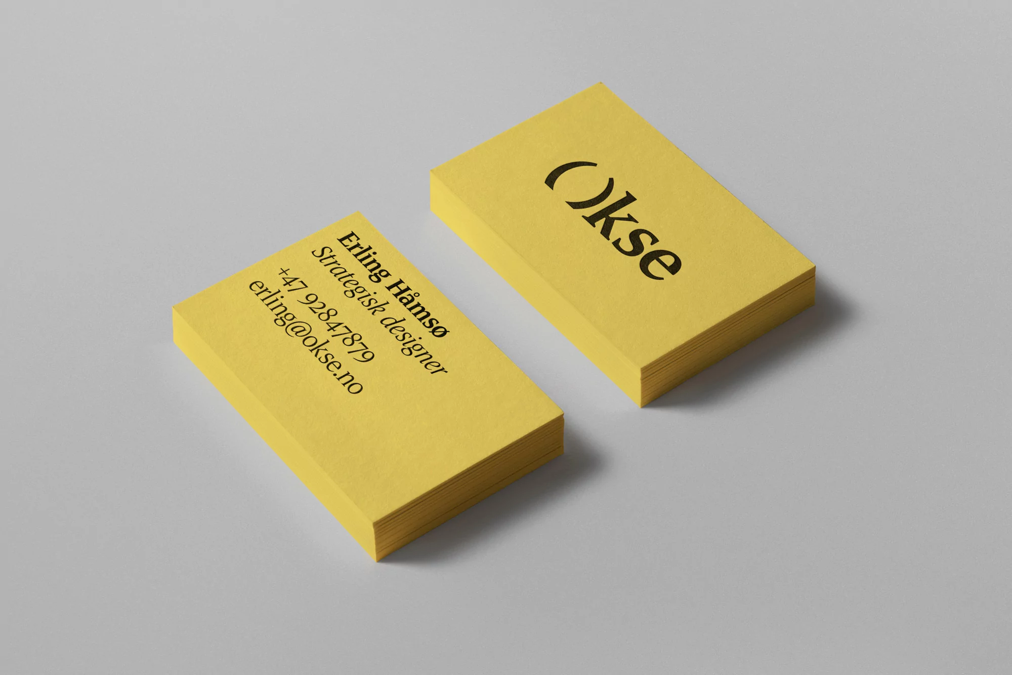 Two stacks of yellow business cards with black text sit on a gray surface in a minimalist composition for corporate branding.