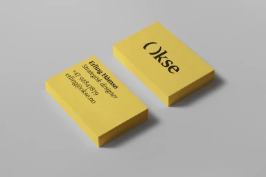 Two yellow business cards displaying black typography for Okse brand identity placed on a neutral grey surface.