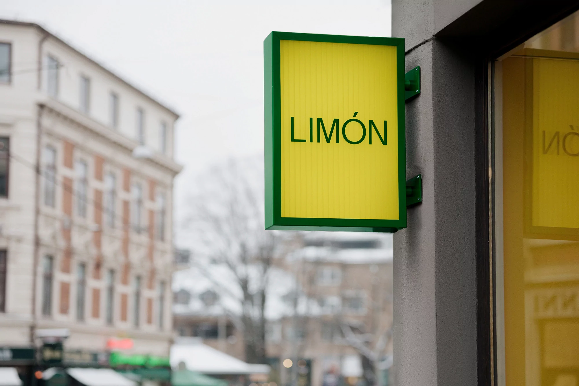 Exterior shot of a yellow and green 'Limón' sign hanging on a building in an urban environment on an overcast day.