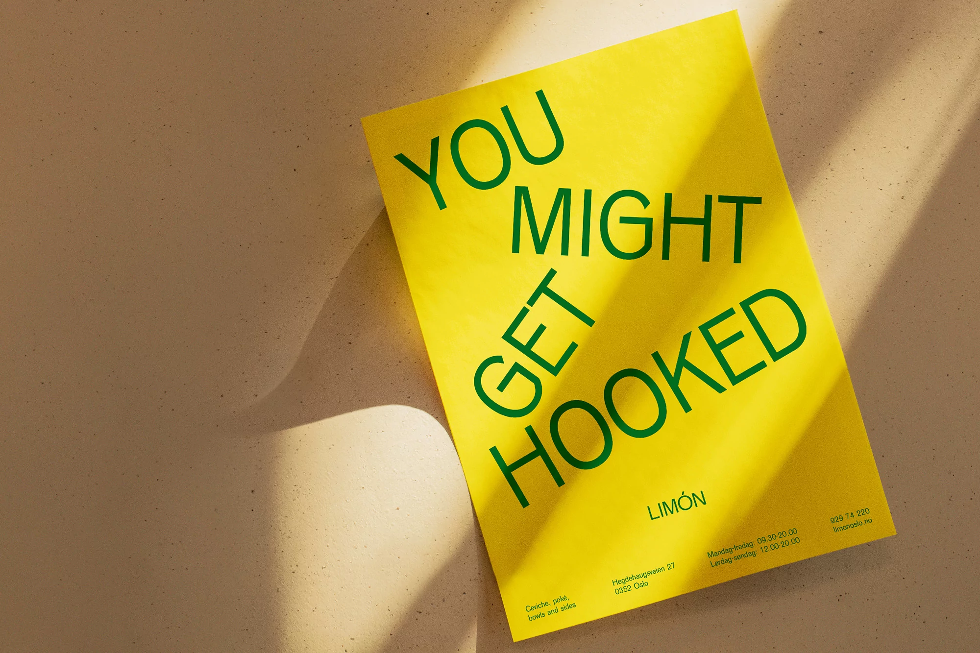 Yellow advertising poster featuring green sans-serif typography on a neutral surface with shadow. Graphic design with bold text.