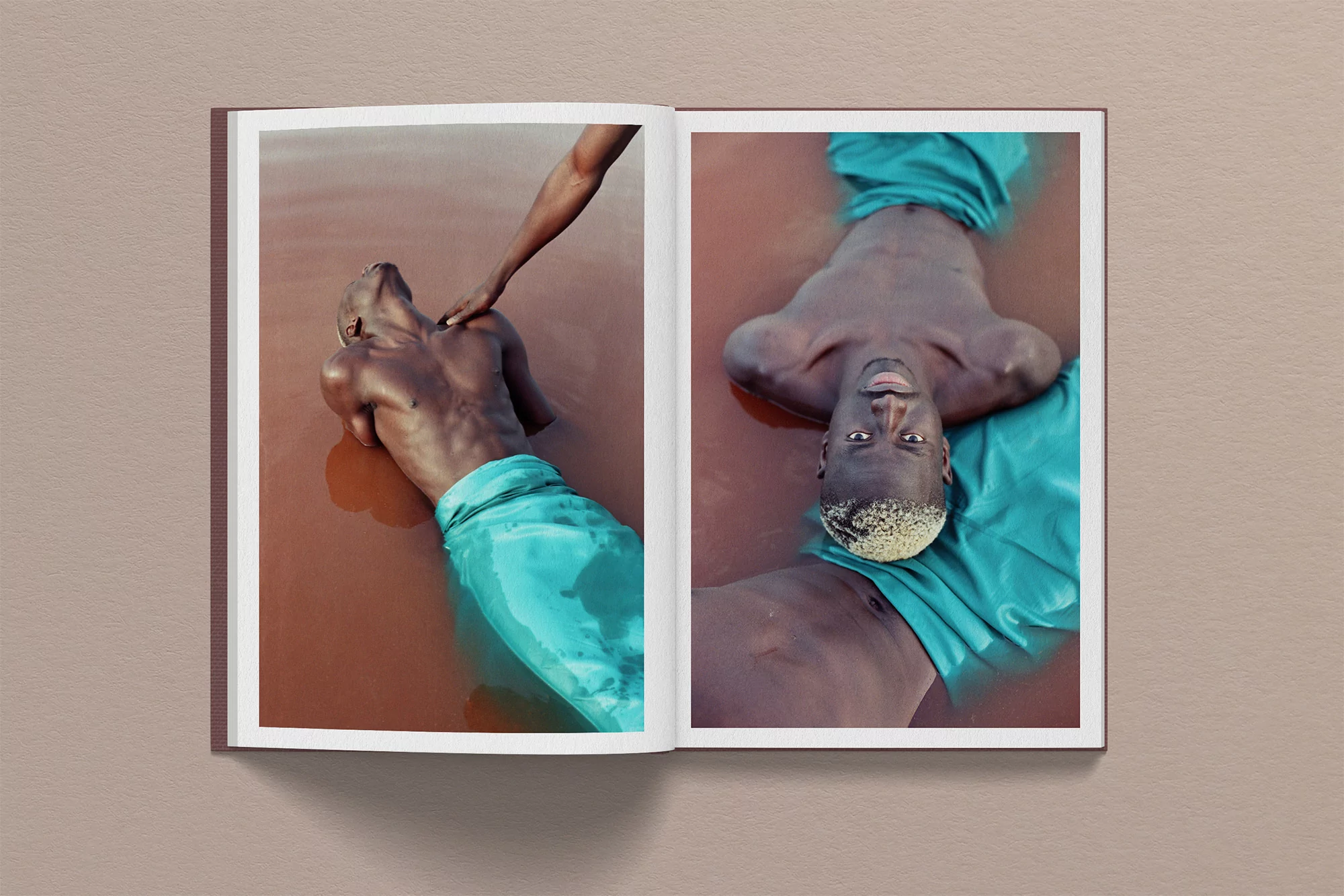Editorial shot of two dark-skinned adult males in water; one is lying down while the other is touching his chest.